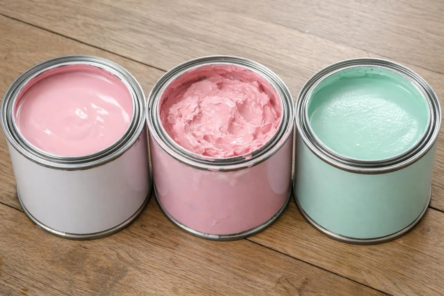 Close-up realistic photograph of three open paint cans showing different textures and finishes of anti-mold bathroom paint, positioned on a wooden surface with visible consistency differences between acrylic and specialized formulas, natural lighting highlighting the paint surfaces without any text or labels